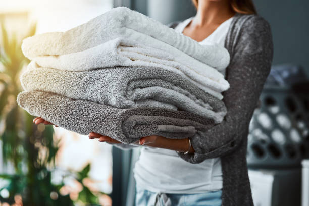 Person holding neatly folded white and grey towels, demonstrating a method for a luxurious bathroom.